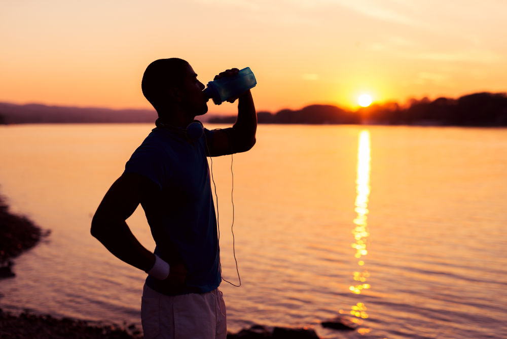 Sportlicher Mann trinkt bei Sonnenuntergang